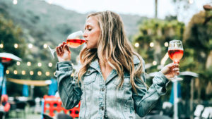 Alkoholgehalt im Wein -Frau trinkt aus einem Weinglas einen Schluck Rosé, während sie in der anderen Hand das nächste Glas bereithält.