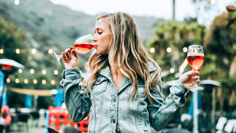 Alkoholgehalt im Wein -Frau trinkt aus einem Weinglas einen Schluck Rosé, während sie in der anderen Hand das nächste Glas bereithält.
