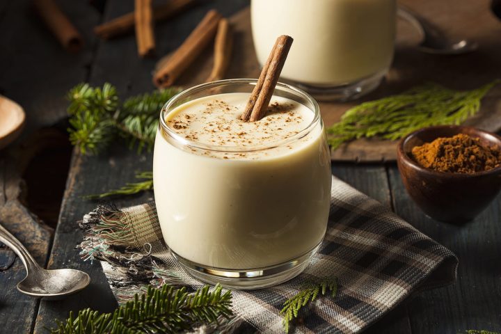 Amerikanischer Eggnog mit Zimtstange auf dunklem Hintergund und Tannenzweigen