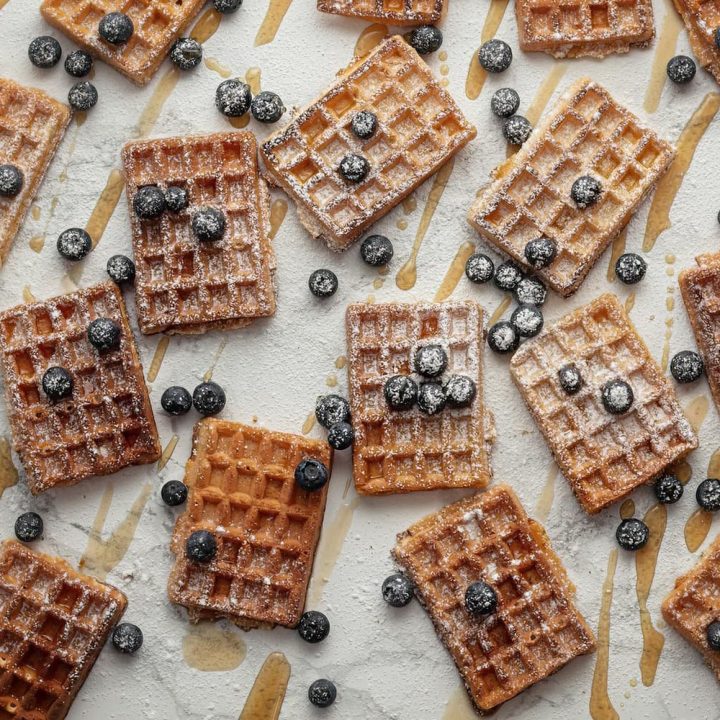 Eine vielzahl belgischer Waffeln mit Ahornsirup und Heidelbeeren auf einem weißen Untergrund