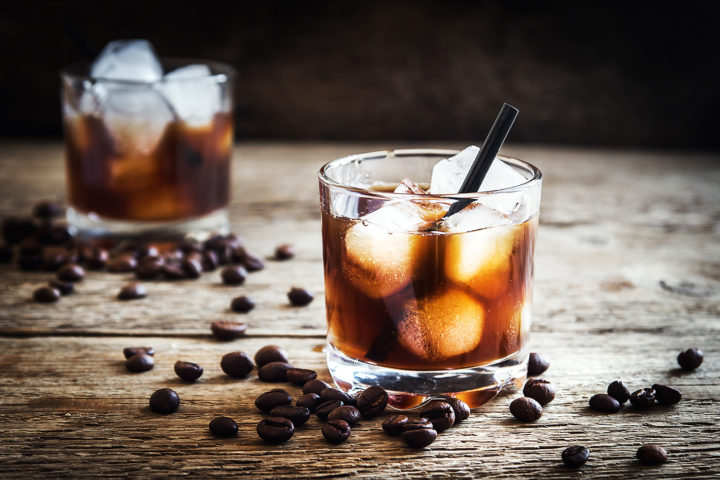 Classic Black Russian cocktail served in an old fashioned glass with ice cubes and coffee beans on a wooden board