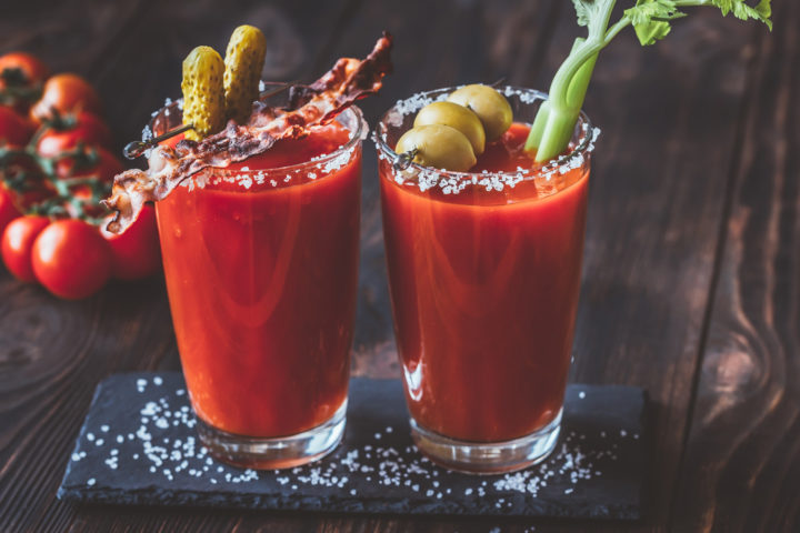 Two Bloody Marys garnished with celery, olives, pickles and bacon.