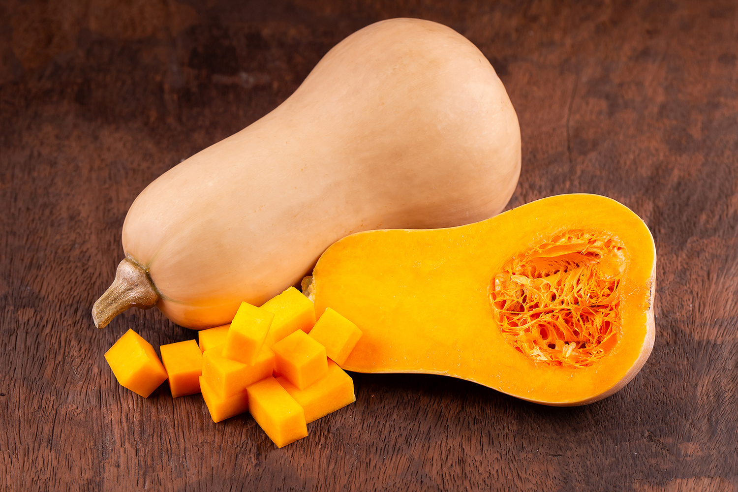 Whole and cut butternut on a wooden table with orange pulp and core