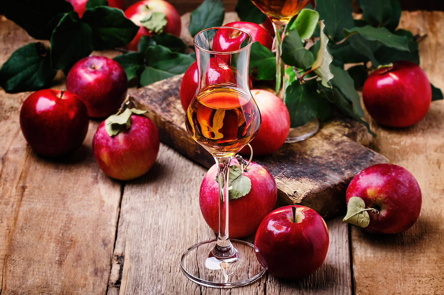 A glass of calvados surrounded by red apples on a wooden background