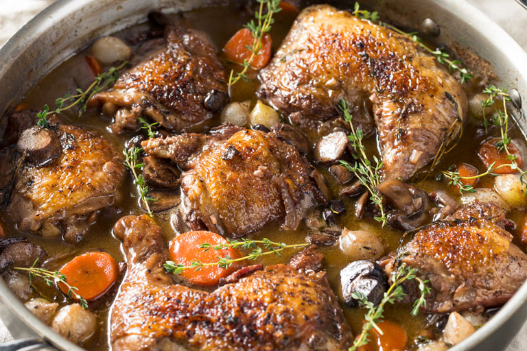Close up of coq au vin with thyme sprigs and pinot noir sauce