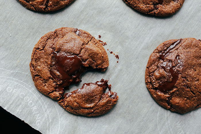 Dark chocolate chip cookie with liquid chocolate center on white baking paper.