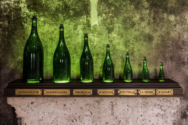 Sieben Champagnerflaschen in einem Keller eines Champagnerhauses in Reims (Frankreich). Absteigend nach ihrer Größe sortiert aufgereiht.