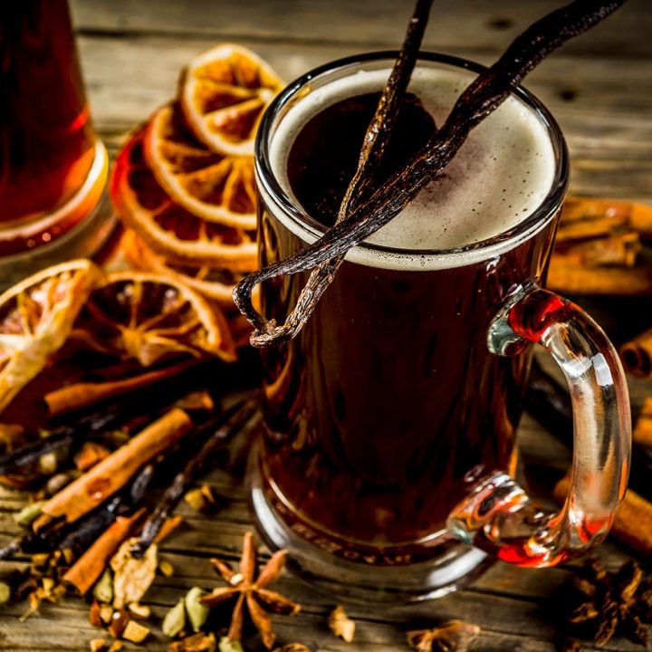 Ein Krug mit Glühbier und winterlichen Gewürzen auf einem hölzernen Brett serviert.