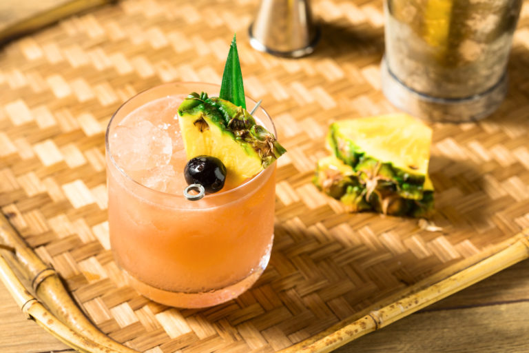 Ein original Mai Tai Cocktail mit Rum und einer Ananasscheibe als Deko auf einem Bambustablett