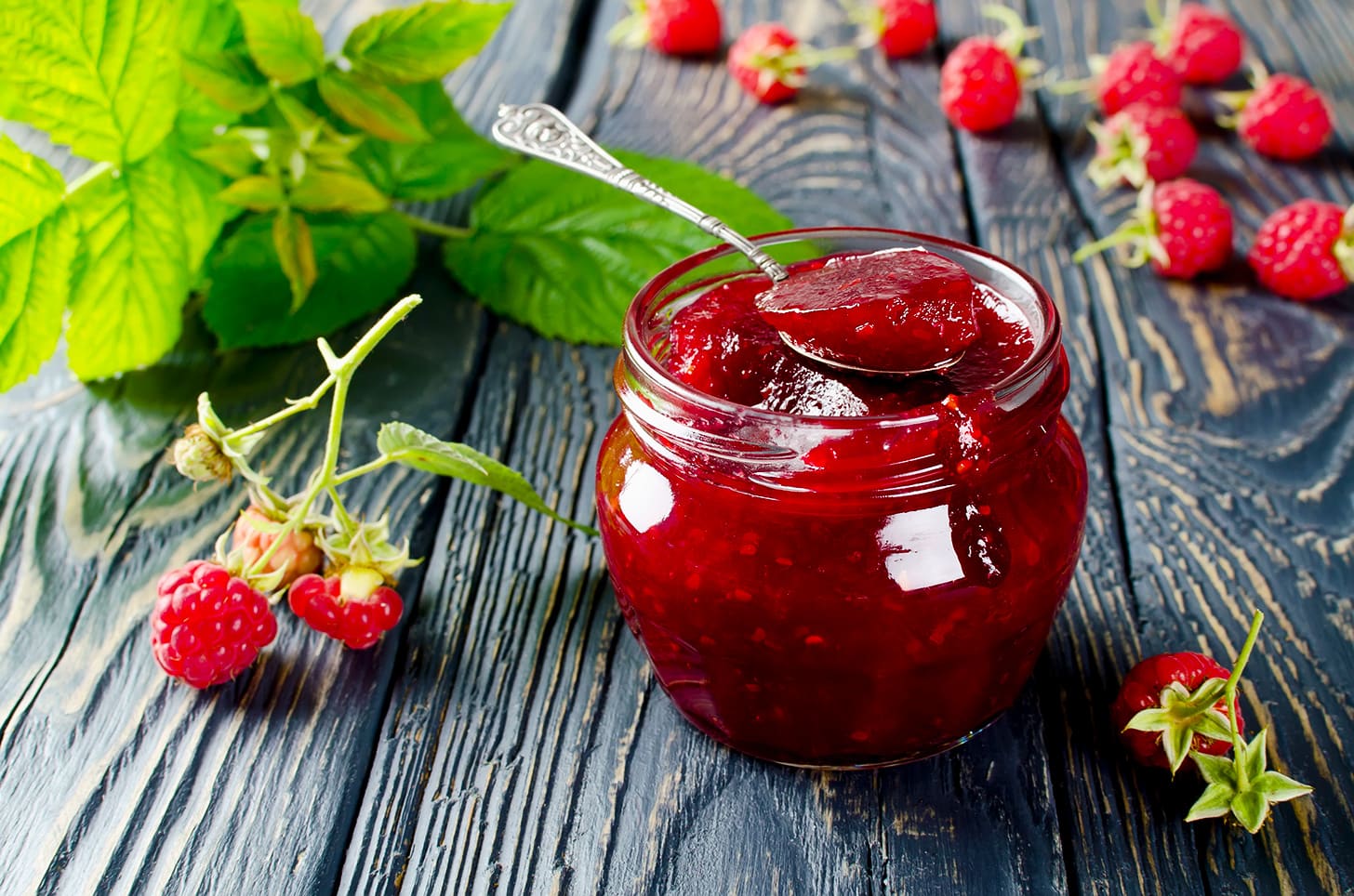 A jar of raspberry jam with fresh fruit on a wooden board