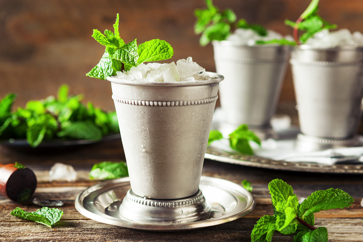 Mint julep cocktails with whiskey, mint and ice in silver cups on a wooden tray