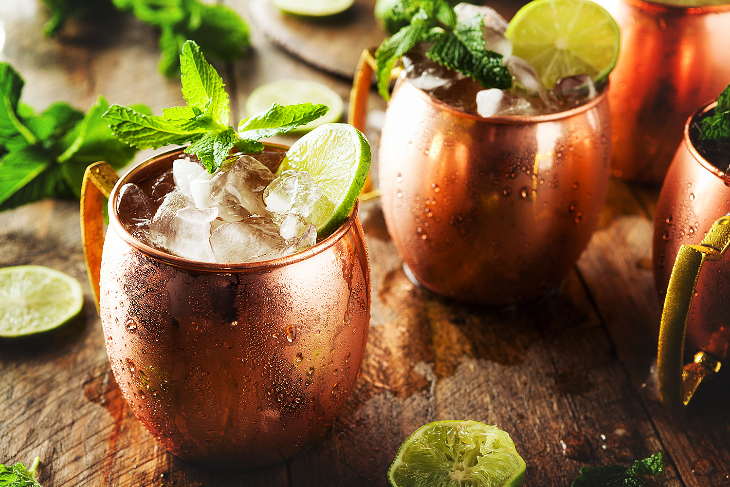 Moscow Mule cocktails with vodka, mint and lime in copper mugs on a wooden board