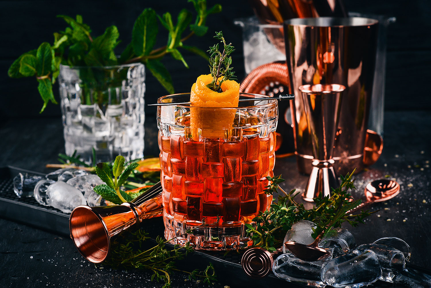 Negroni Aperitif mit Orangenzeste und Thymianzweig vor dunklem Hintergrund