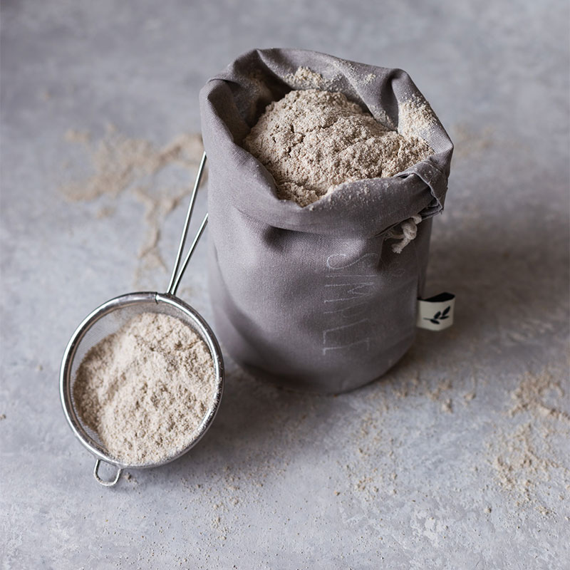 Wheat flour for waffle batter in a small, open cloth flour bag with a sifter next to it.