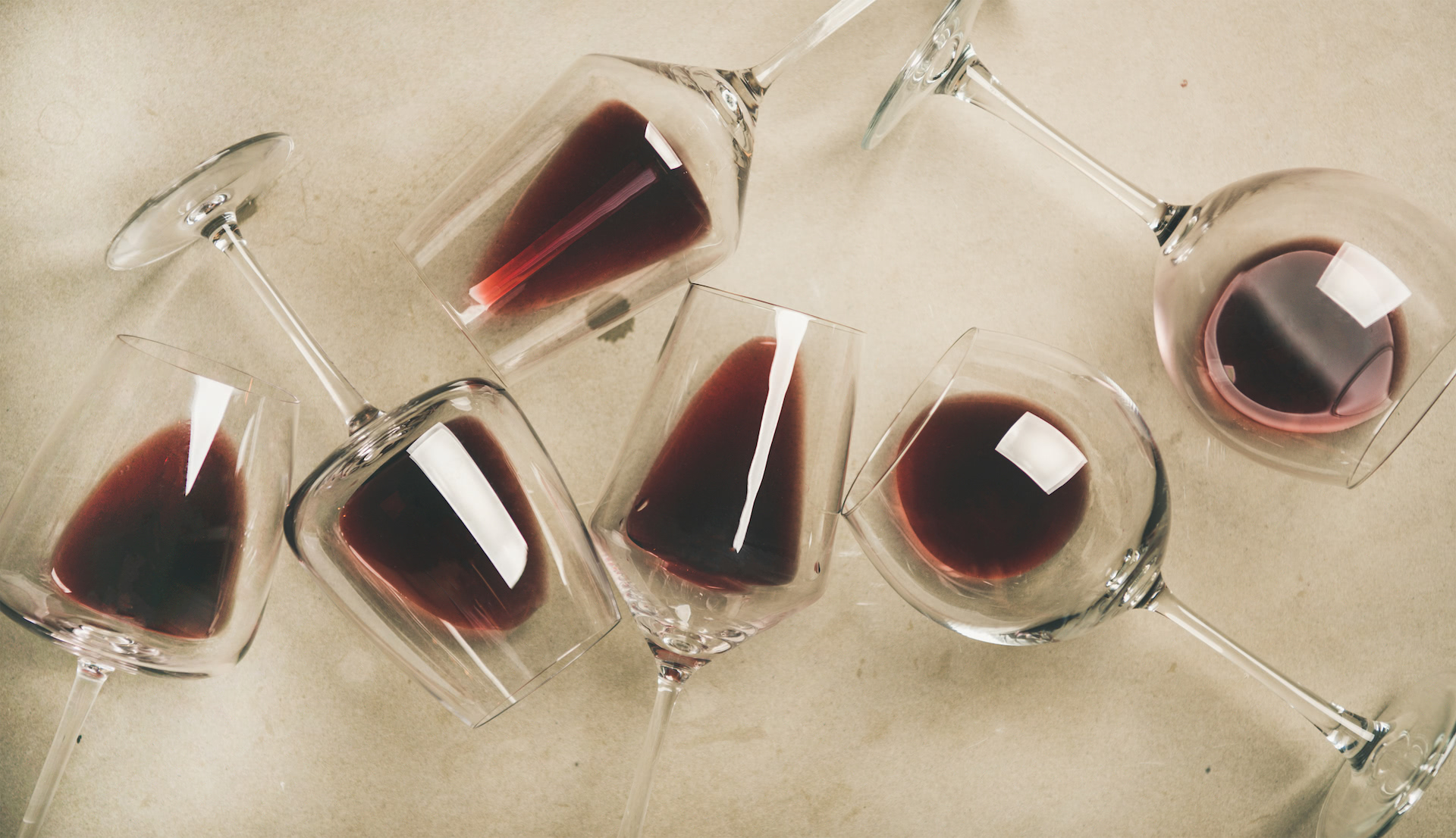 Filled red wine glasses lying on a light stone background