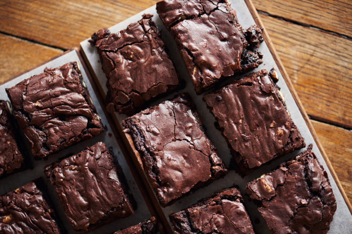 Saftige Brownies auf einem Backblech mit Backpapier vor einem hölzernen Hintergrund