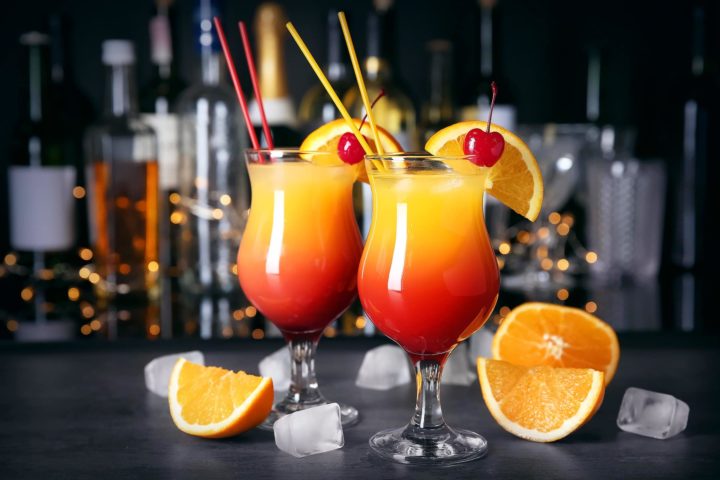 Zwei Gläser Sex on the Beach Cocktail vor dunklem Hintergrund, Orangen und Eiswürfel