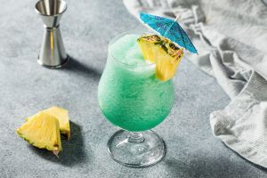 Swimming Pool / Blue Hawaiian Cocktail mit Ananas, Rum und Wodka auf grauem Hintergrund mit einem Jigger und einem Küchenhandtuch