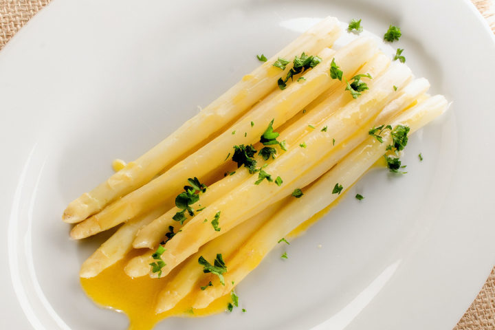 Gekochter weißer Spargel mit Buttersauce und Petersilie auf einer weißen Servierplatte