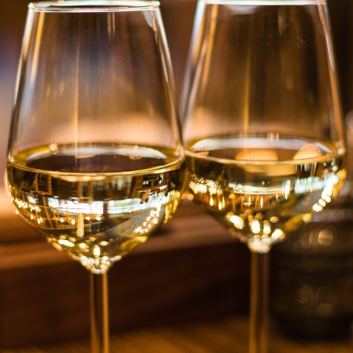 Nahaufnahmen von zwei Weingläsern mit Weißwein auf einem gedeckten Tisch