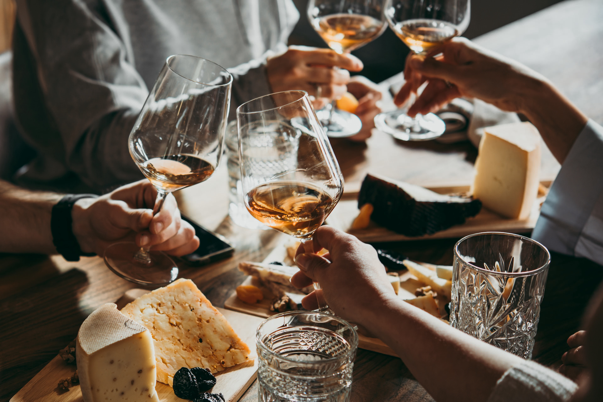 A group of four friends toasting with white wine and enjoying a cheese platter.