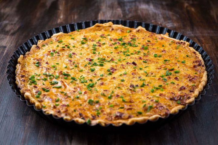 Zwiebelkuchen mit Speck und Schnittlauch in Backform auf dunklem Untergrund